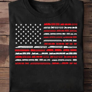Könnte beinhalten: Schwarzes T-Shirt mit einem Design der amerikanischen Flagge. Die Sterne sind weiß, und die Streifen bestehen aus roten und weißen Zugillustrationen. Ein einzigartiges Design für Eisenbahnfans und Patrioten.