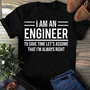 Pode incluir: Camiseta preta com texto branco: "I AM AN ENGINEER TO SAVE TIME LET'S ASSUME THAT I'M ALWAYS RIGHT". A camiseta está sobre uma superfície de madeira, com sapatos castanhos e jeans azuis.