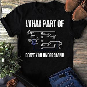 May include: Black t-shirt featuring the text "WHAT PART OF DON'T YOU UNDERSTAND" and a circuit diagram. The image includes blue jeans and brown shoes, indicating a relaxed, everyday look.