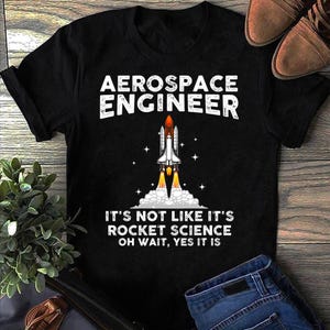 Peut inclure: T-shirt noir avec l'inscription "AEROSPACE ENGINEER" et un dessin de fusée. En dessous, le texte dit "IT'S NOT LIKE IT'S ROCKET SCIENCE OH WAIT, YES IT IS."