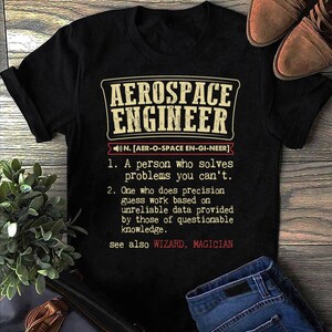 Könnte beinhalten: Schwarzes T-Shirt mit dem Text "AEROSPACE ENGINEER" in einem rechteckigen Design. Die Definition eines Luft- und Raumfahrtingenieurs ist unter dem Titel aufgeführt. Das Shirt wird mit einer blauen Jeans und braunen Schuhen kombiniert.