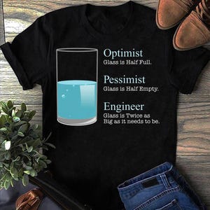 May include: Black t-shirt with a humorous graphic about perspectives. The design features a glass half-full of blue liquid, with text stating "Optimist," "Pessimist," and "Engineer," each with a different interpretation of the glass.
