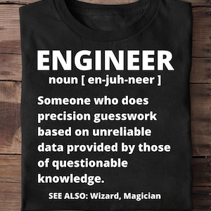 May include: Black t-shirt with the word "ENGINEER" in large white letters. The definition of engineer is printed below, including the pronunciation and a humorous description. The shirt also says "SEE ALSO: Wizard, Magician."