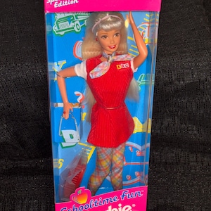 May include: Special Edition Schooltime Fun Barbie doll in original packaging. The doll wears a red corduroy dress with a white collared shirt and plaid pants. The box is pink and blue with the Barbie logo and a school bus graphic.