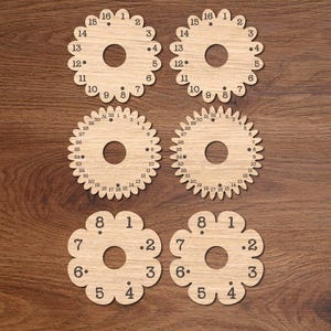 Puede incluir: Seis marcadores de punto de madera en varias formas florales y de engranajes. Cada marcador está cortado con láser con números alrededor de los bordes. Los números van del 1 al 32 y del 1 al 16. El fondo es una superficie de madera oscura.