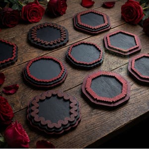 Peut inclure: Un ensemble de huit dessous de verre sombres avec des bords rouges festonn&eacute;s ou octogonaux. Les dessous de verre sont dispos&eacute;s sur une surface en bois avec plusieurs roses rouges et des p&eacute;tales &eacute;parpill&eacute;s. Un logo indique Doodles Doodles Studio.