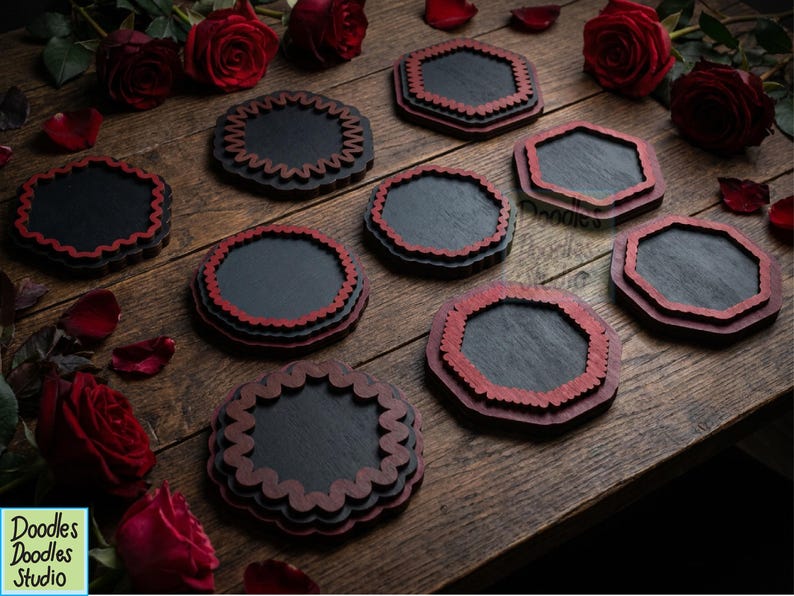 Peut inclure: Un ensemble de huit dessous de verre sombres avec des bords rouges festonn&eacute;s ou octogonaux. Les dessous de verre sont dispos&eacute;s sur une surface en bois avec plusieurs roses rouges et des p&eacute;tales &eacute;parpill&eacute;s. Un logo indique Doodles Doodles Studio.