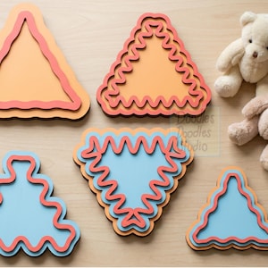 Peut inclure: Cinq formes en bois superpos&eacute;es, triangulaires et abstraites, avec des bords ondul&eacute;s dans des tons orange, bleu clair et rouge. Deux petits ours en peluche sont plac&eacute;s pr&egrave;s des formes. Le texte Doodles Doodles Studio est visible.