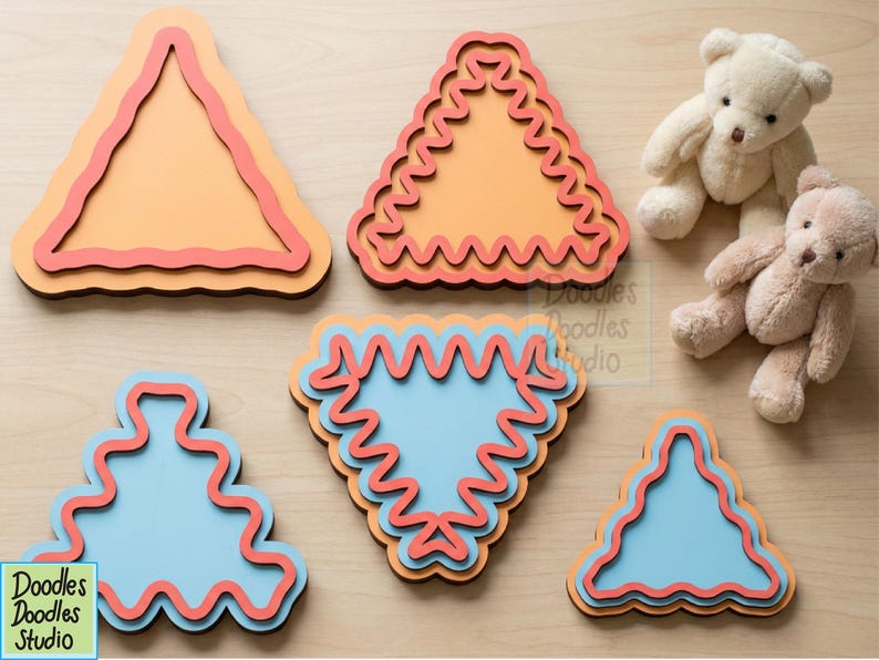 Peut inclure: Cinq formes en bois superpos&eacute;es, triangulaires et abstraites, avec des bords ondul&eacute;s dans des tons orange, bleu clair et rouge. Deux petits ours en peluche sont plac&eacute;s pr&egrave;s des formes. Le texte Doodles Doodles Studio est visible.