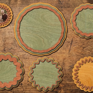 Peut inclure: Un ensemble de six cadres et plaques circulaires en bois superpos&eacute;s avec des bords festonn&eacute;s dans des tons vert sauge, terre cuite et bois naturel. Un cadre contient une photographie de famille, tandis que les autres sont vides.