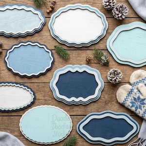 Peut inclure: Une collection de huit plaques en bois aux bords festonn&eacute;s dans diverses nuances de bleu, blanc et bleu sarcelle clair. Les plaques pr&eacute;sentent des designs superpos&eacute;s avec des finitions lisses, dispos&eacute;es avec des pommes de pin et des moufles.