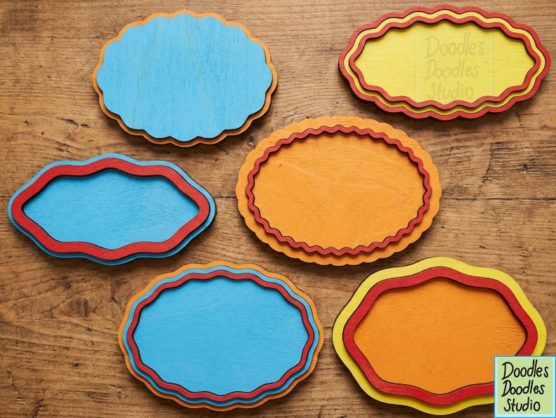 Peut inclure: Six plaques en bois aux bords festonn&eacute;s de couleur bleue, jaune et orange. Les plaques pr&eacute;sentent des motifs superpos&eacute;s avec des bordures rouges ou jaunes. Une plaque jaune porte le texte Doodles Doodles Studio et un logo affiche ce texte.