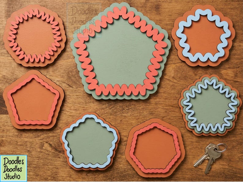 Peut inclure: Un ensemble de sept formes g&eacute;om&eacute;triques superpos&eacute;es dans des tons vert sauge, orange terre cuite et bleu clair. Chaque pi&egrave;ce pr&eacute;sente un bord ondul&eacute; ou festonn&eacute;. Un petit porte-cl&eacute;s en m&eacute;tal avec deux cl&eacute;s argent&eacute;es est plac&eacute; en bas &agrave; droite.