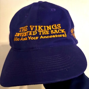 Vikings Sports Cap in purple and gold. “The Vikings Invented the Sack (Go Ask Your Ancestors)” on front. Vikings Dragon Ship Logo on side.