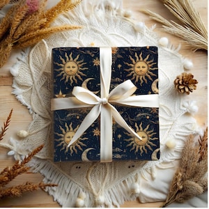 May include: A gift wrapped in dark blue wrapping paper with a gold and white celestial pattern. The paper features repeating images of the sun and moon with stars and clouds. The gift is tied with a white satin ribbon.