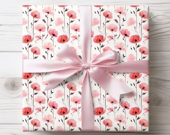 May include: A gift box wrapped in white paper with a pink floral pattern. The paper features a repeating design of pink and red watercolor poppies with green stems. The box is tied with a pink satin ribbon.