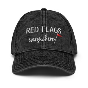 May include: A black distressed denim baseball cap with white embroidery that reads "RED FLAGS everywhere" and a small red flag graphic.