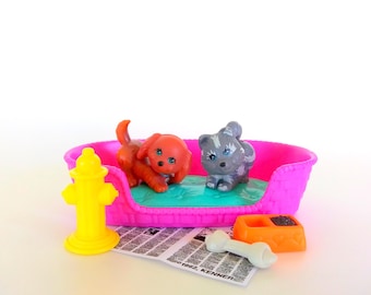 May include: A set of two small plastic animal figurines, one orange and one gray, inside a bright pink plastic pet bed. The set includes a yellow fire hydrant, an orange food bowl with black food, a white bone, and a small paper with 1992 Kenner text.