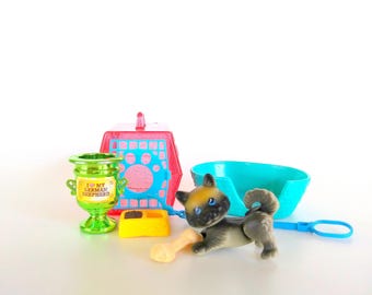 Pode incluir: Um conjunto de brinquedos em miniatura com uma pequena figura de cão castanho e preto, um troféu verde brilhante com o texto I LOVE MY GERMAN SHEPHERD, uma transportadora rosa, uma cama turquesa, uma taça amarela e um osso de brinquedo bege.