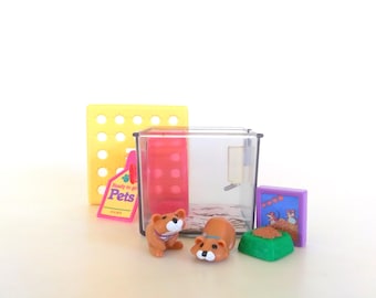 May include: A miniature clear plastic pet enclosure containing a pink exercise wheel and water bottle. Included are two small brown animal figurines, a green food bowl, a yellow perforated panel, a pink tag labeled Ready to go Pets, and a purple frame.