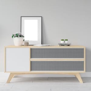May include: A light wood cabinet with two drawers and a white door. The cabinet has a gray slatted front and sits on four legs. A black picture frame, two small potted plants, and a stack of books are on top of the cabinet.