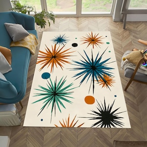 May include: A rectangular area rug with a cream background features a mid-century modern design. The rug showcases starburst patterns in teal, orange, and black, with small dots of color scattered across the surface. The rug is placed on a hardwood floor.