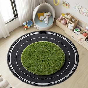 Könnte beinhalten: Ein runder Teppich mit Straßendesign. Der äußere Ring ist schwarz mit weißen gestrichelten Linien, die eine Straße darstellen. Die Mitte ist ein grüner Kreis, der Gras simuliert. Der Teppich liegt auf einem hellen Holzboden.