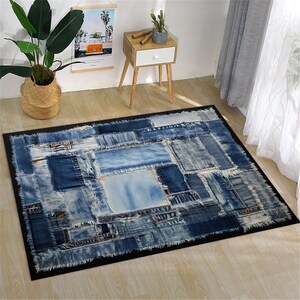 May include: Rectangular denim rug with a patchwork design. The rug features various shades of blue denim patches, creating a textured appearance. The rug is bordered by a black trim and is placed on a light-colored wooden floor.