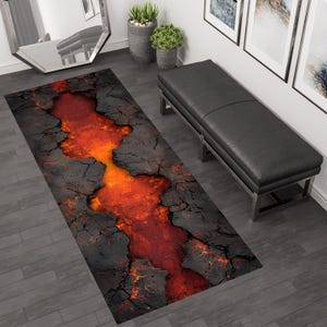 May include: A rectangular rug with a dramatic design. The rug has a cracked, dark grey surface with a vibrant orange and red lava-like pattern through the centre. The rug is placed on a grey wooden floor.