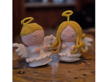 May include: Two crocheted angel figurines with pale pink faces, white dresses, and white wings. One angel has short yellow hair and a halo, while the other has long yellow hair and a halo. The text PDF PATTERN is visible at the bottom.