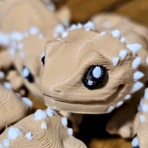 Peut inclure: Gros plan sur un groupe de petites figurines imprimées en 3D de couleur beige avec des accents blancs. Les figurines ont de grands yeux noirs et une surface texturée.