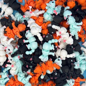 Op de afbeelding: Een grote verzameling kleurrijke, gearticuleerde plastic speelgoed. De speelgoedjes staan in verschillende poses en hebben verschillende kleuren, waaronder zwart, wit, oranje, blauw en groen.