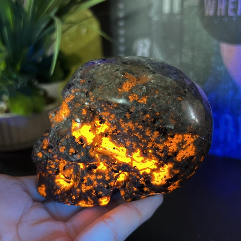 May include: A skull-shaped decorative object with a dark gray and orange speckled pattern. The skull has a glowing orange interior, creating a striking contrast. The object is likely made of stone or a similar material.