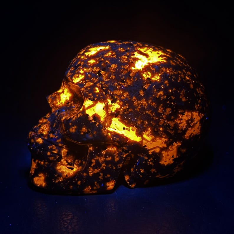 May include: A glowing skull sculpture with a dark background. The skull is made of a dark material with orange and yellow highlights, creating a striking contrast. The sculpture is a unique decorative item.