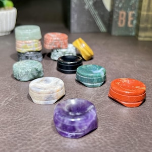 Pode incluir: Uma coleção de pequenas caixas decorativas de pedra em várias cores e padrões. As caixas são redondas com um topo rebaixado e são feitas de materiais como ametista, ágata e jaspe. A imagem mostra a beleza natural e as texturas únicas das pedras.