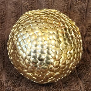 May include: A gold sphere covered in hundreds of small, round, gold push pins.
