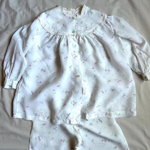 May include: A white pajama top with a floral print and a lace collar. The top has a button-up front and long sleeves. The matching pajama bottoms are also white with a floral print.