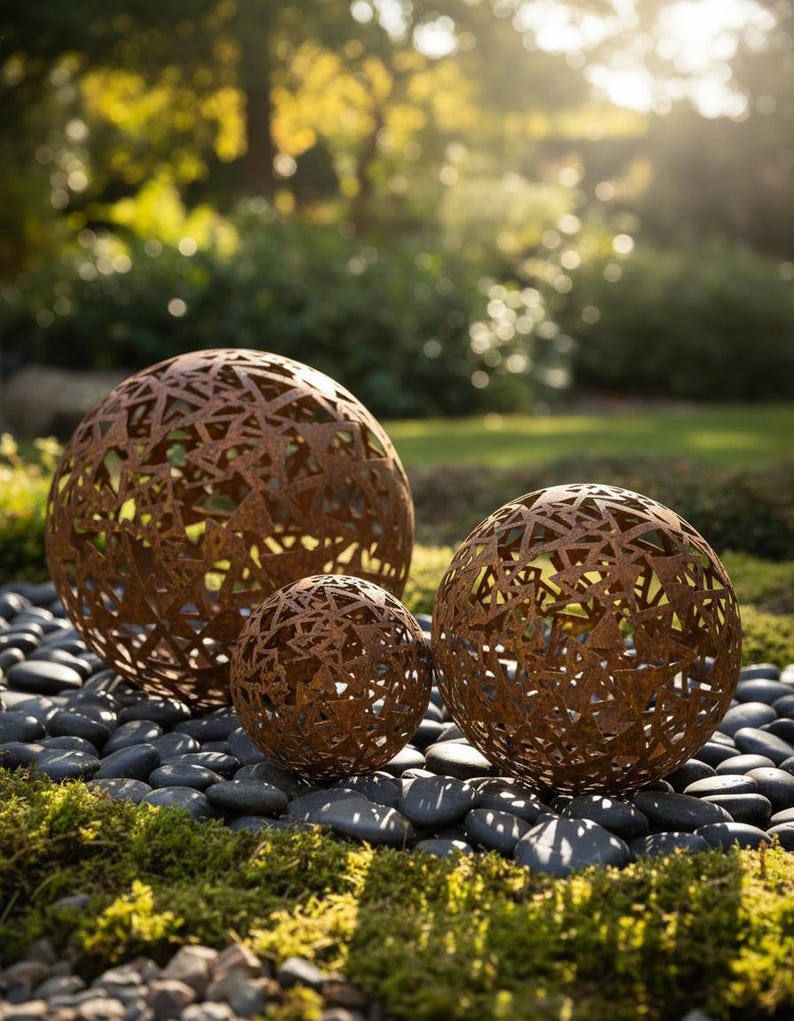 May include: Three decorative metal spheres with a rusted finish, of varying sizes, are displayed on a bed of black pebbles and moss. The spheres feature intricate cut-out patterns. These garden ornaments add a unique touch to outdoor spaces, with a natural aesthetic.