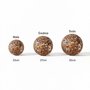 May include: Three bronze-coloured metal spheres with decorative cut-out patterns. The spheres are of varying sizes, with diameters of approximately 23 cm, 27 cm, and 35 cm. The image includes the text "Mała", "Średnia", and "Duża".