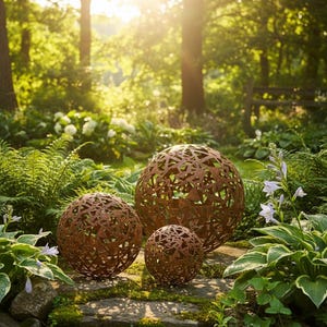 May include: Three decorative metal spheres with intricate cut-out designs, varying in size, rest on a stone surface amidst lush greenery. The spheres have a rustic, weathered appearance, adding a touch of natural elegance to the garden setting.