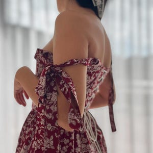 May include: A red and white floral print dress with a fitted bodice and a full skirt. The dress has a sweetheart neckline and is strapless. The sleeves are tied at the shoulders with matching fabric.