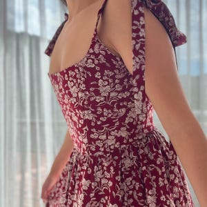 May include: A red floral print dress with thin straps that tie at the shoulders. The dress has a fitted bodice and a full skirt.