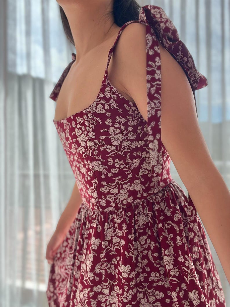 May include: A red floral print dress with thin straps that tie at the shoulders. The dress has a fitted bodice and a full skirt.