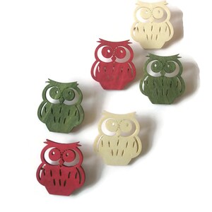 May include: Five wooden owl ornaments in red, green, and cream colors. The owls have large eyes and are cut out in a simple design.