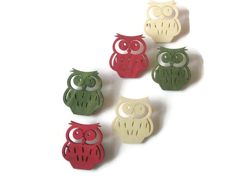 May include: Five wooden owl ornaments in red, green, and cream colors. The owls have large eyes and are cut out in a simple design.