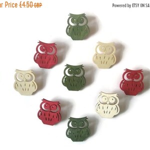 May include: Ten wooden owl cutouts in three colors: red, green, and cream. The owls are all facing forward with their eyes open and have a simple design.