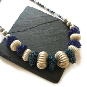 May include: A silver and blue beaded necklace with large, round, silver beads and smaller, blue beads. The necklace is on a black slate surface.