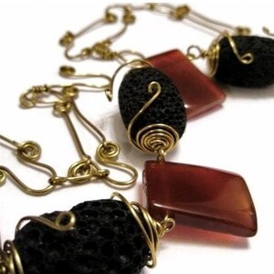 Puede incluir: Un collar con una cadena de oro y cuentas de roca volcánica negra envueltas en alambre dorado. El collar también presenta piedras de cornalina roja.