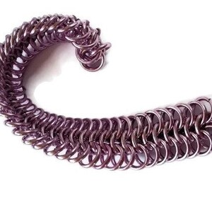 May include: A purple metal chainmail bracelet with a unique design. The bracelet is made of small, interlocking metal rings.