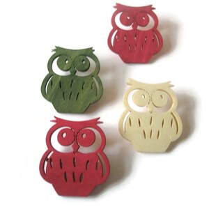 May include: Four wooden owl ornaments in different colors: red, green, cream, and brown. The owls have large eyes and a simple design.